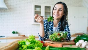 young woman eating a salad on a kitchen counter smiling