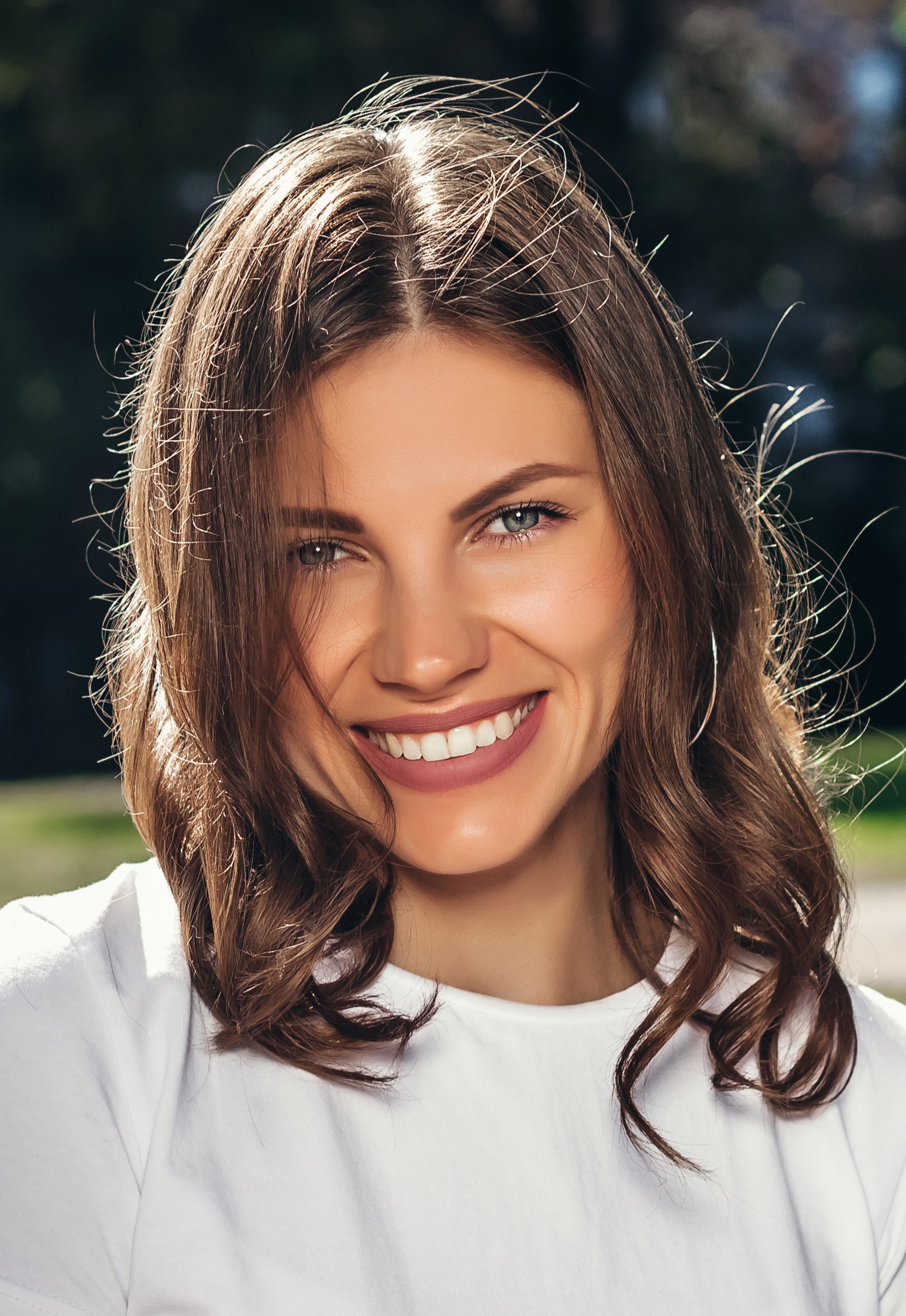 Portrait of a young cute girl in a white T-shirt with a smile in the park. Attractive girl smiling in the park and looking at the camera
