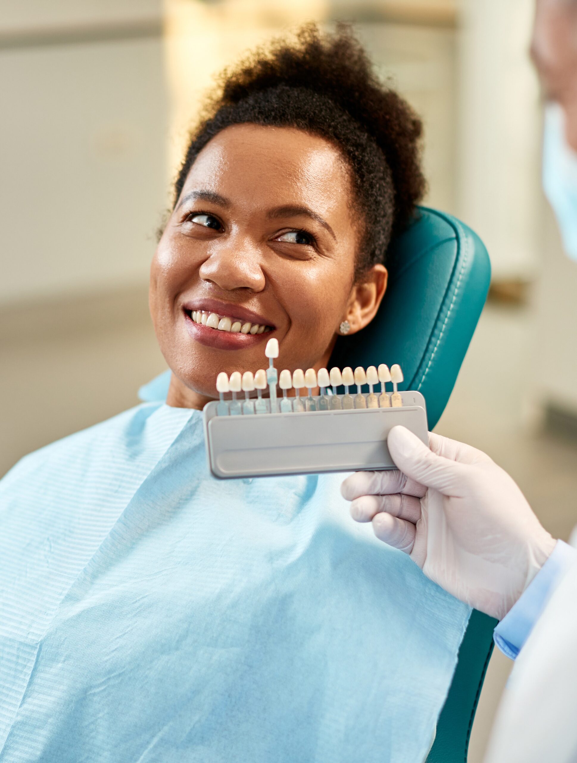Happy black woman and her dentist choosing shade of dental veneers during appointment at dentist's office.