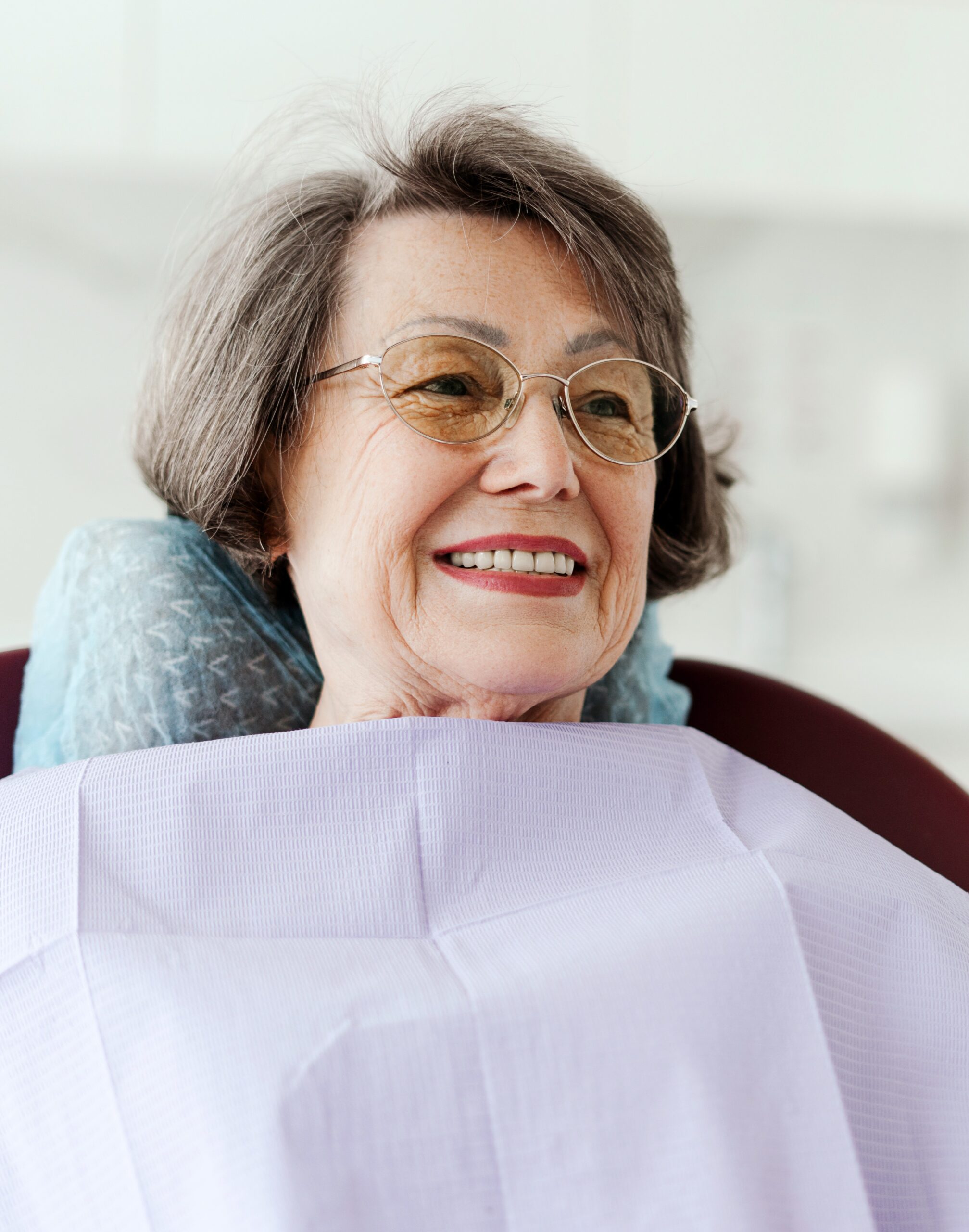 Smiling senior attractive female patient holding mirror looking at teeth while sitting in dental chair in modern dentistry. Concept of dental care, health care