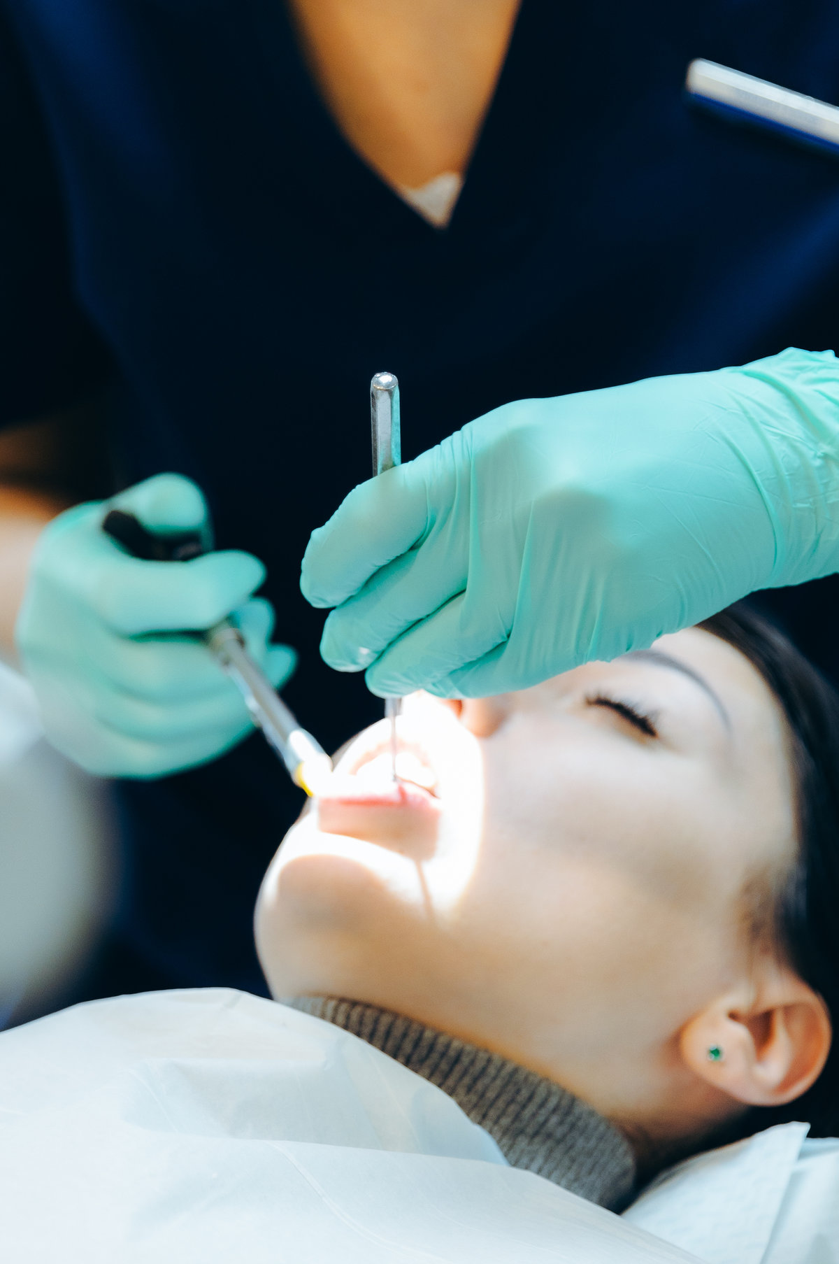 An unrecognizable Caucasian dentist in green latex gloves gives an anesthesia injection to a girl patient using a disposable syringe and a dental mirror in a private clinic, side view very close-up. Concept for treatment of gums and teeth, dentist's day.