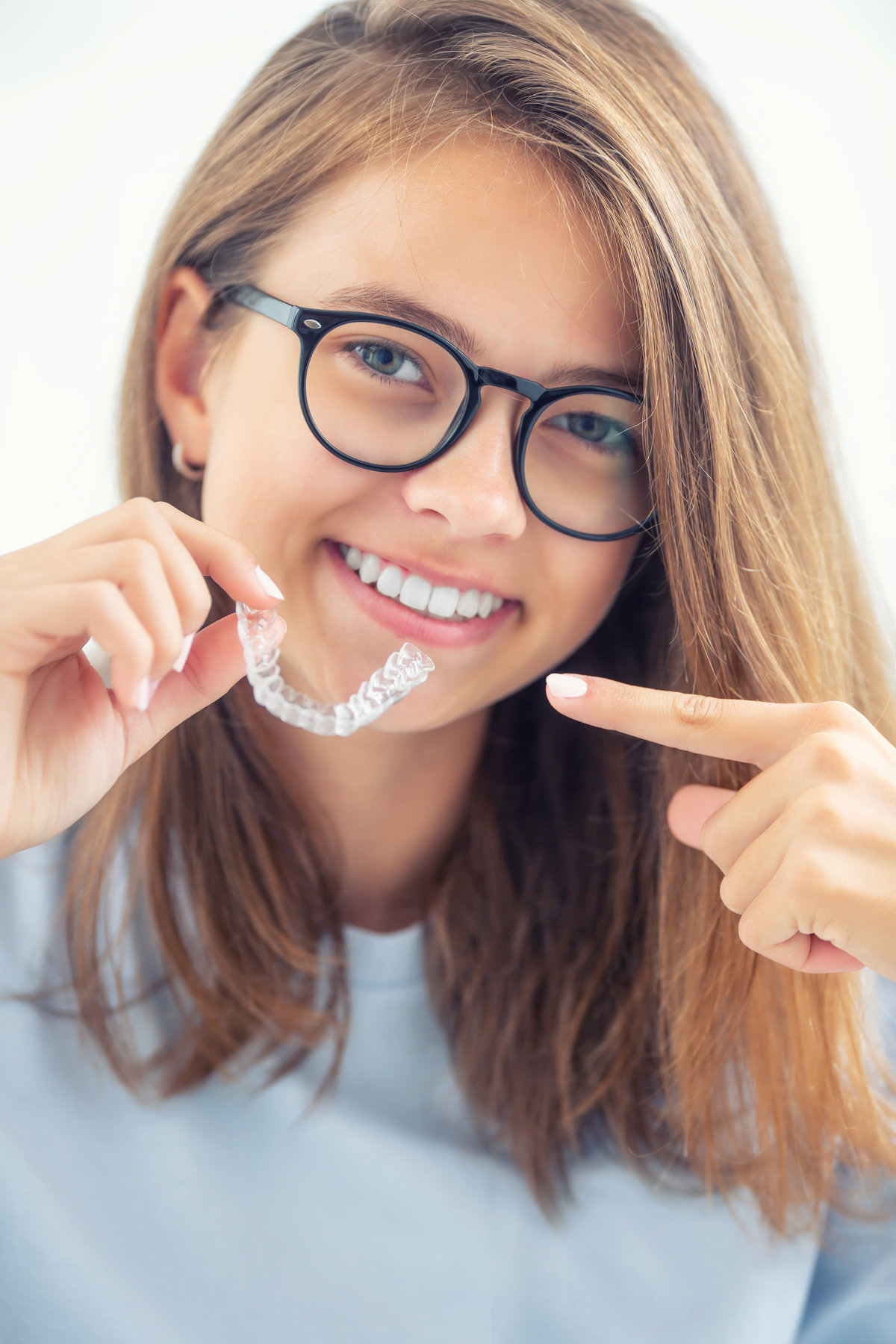 Dental invisible braces or silicone trainer in the hands of a young smiling girl. Orthodontic concept - Invisalign.