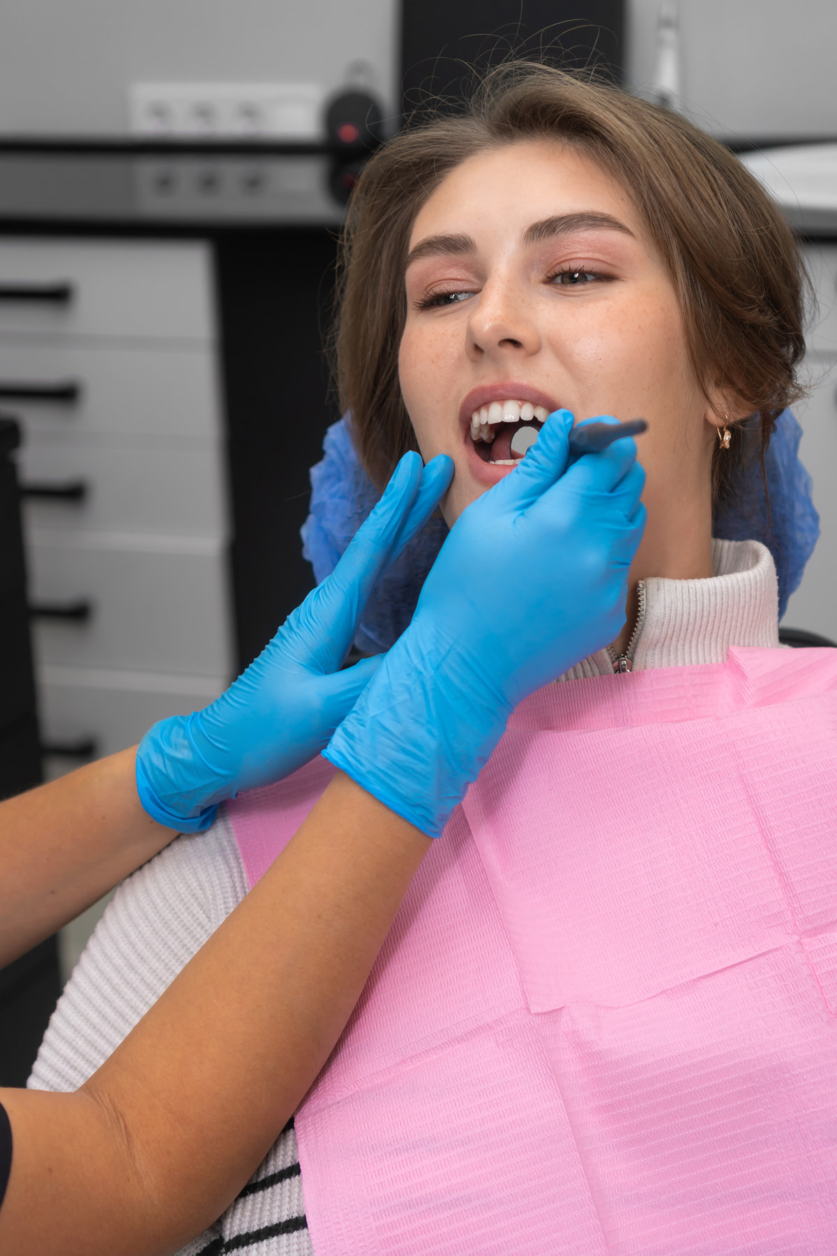 Close-up dentist examines the patient's teeth using a dental mirror. Young beautiful woman at a dentist appointment. Concept of oral care. Vertical photo