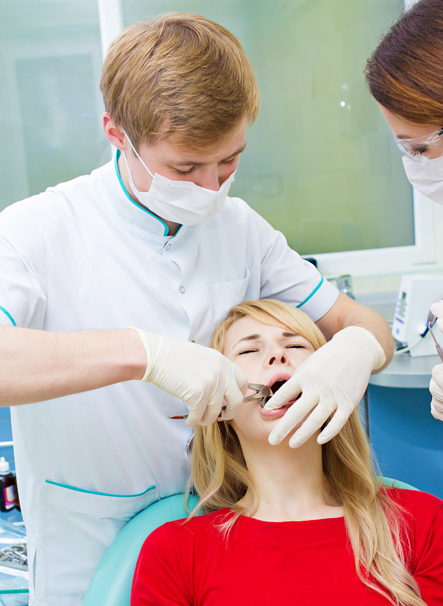 Closeup young woman at dentist clinic office. Male doctor and assistant performing extraction procedure with forceps removing patient tooth. Healthcare dentistry medicine concept
