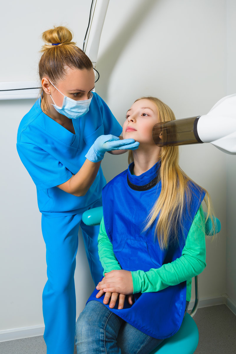 Dentist hands make jaw x-ray image for little girl in dental clinic.